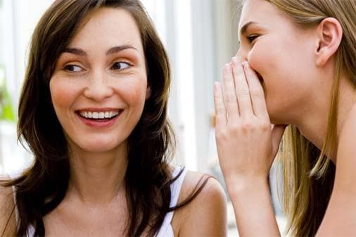 Woman whispering into another's ear